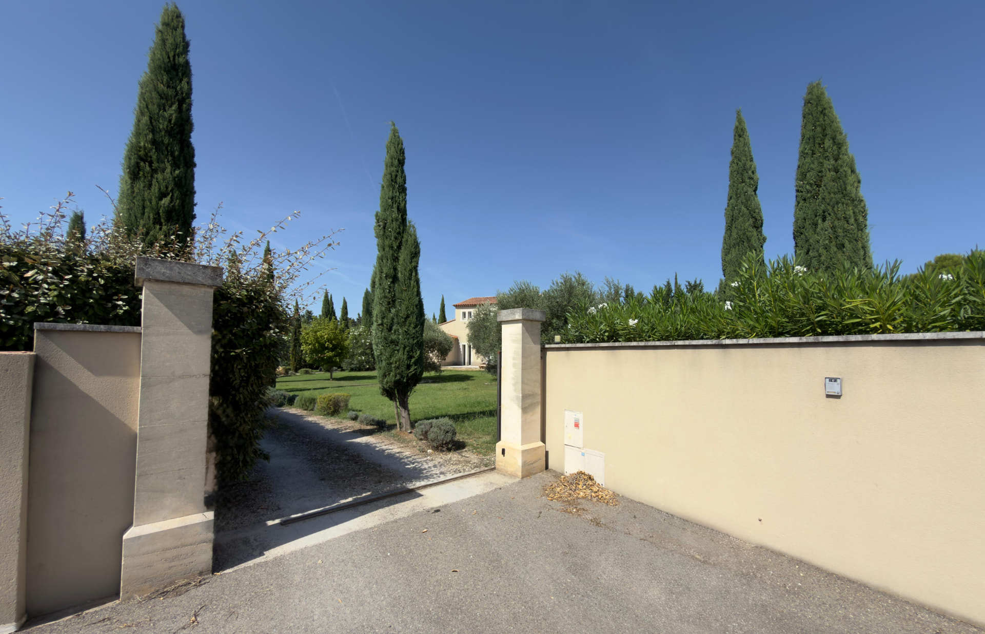 L'entrée de la propriété, avec son portail ouvert entre les murs et les cyprès